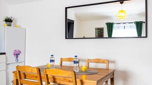Ein Essbereich mit einem Holztisch, zwei Stühlen, einem Kühlschrank und einem Spiegel an der Wand.