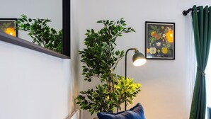 Ein Zimmer mit einer Couch, einer Pflanze, einer Lampe und einem gerahmten Bild an der Wand.