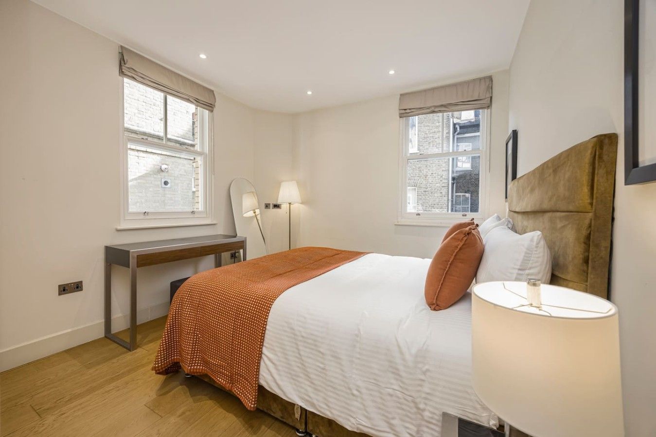 A hotel room with a bed, bedside table, lamp, and two windows.