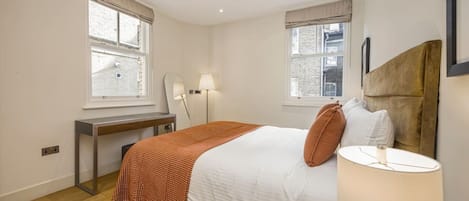 A hotel room with a bed, bedside table, lamp, and two windows.