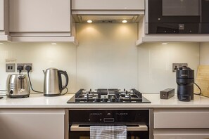 A modern kitchen with a built-in stove, kettle, and coffee maker. - Fitzrovia 1BR Retreat | Near Soho & Tube-9 (Greater London)