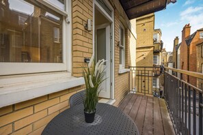 A balcony with a potted plant, a small round table, and a black metal railing. - Fitzrovia 1BR Retreat | Near Soho & Tube-9 (Greater London)