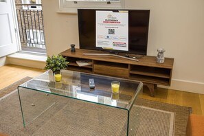 A living room with a glass coffee table, a flat-screen TV on a wooden stand, a small potted plant, and a glass candle. - Fitzrovia 1BR Retreat | Near Soho & Tube-9 (Greater London)