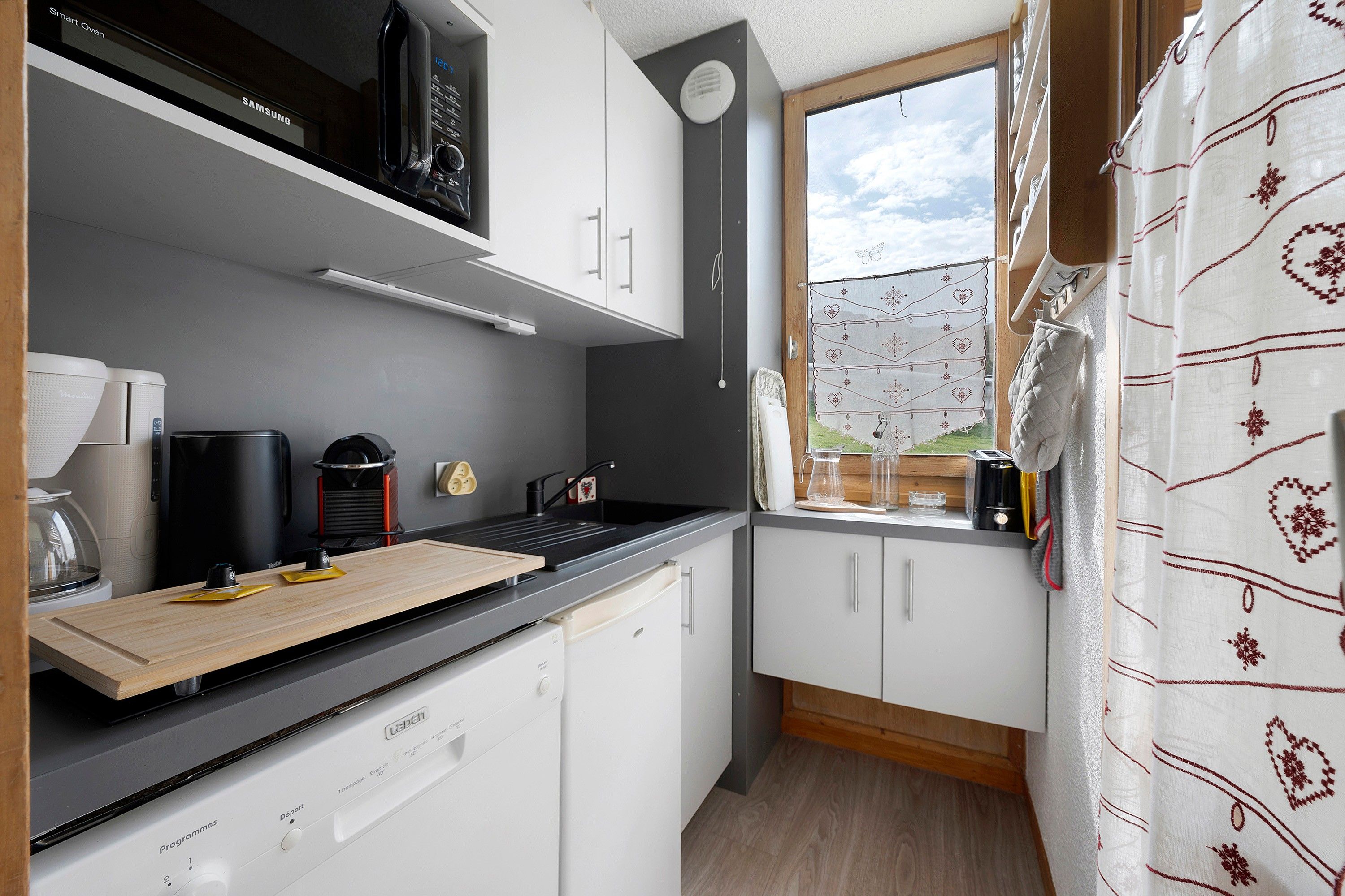 A compact kitchen with white cabinets, a black countertop, and a window with a view of greenery.