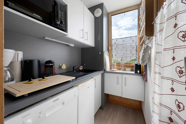 A compact kitchen with white cabinets, a black countertop, and a window with a view of greenery.
