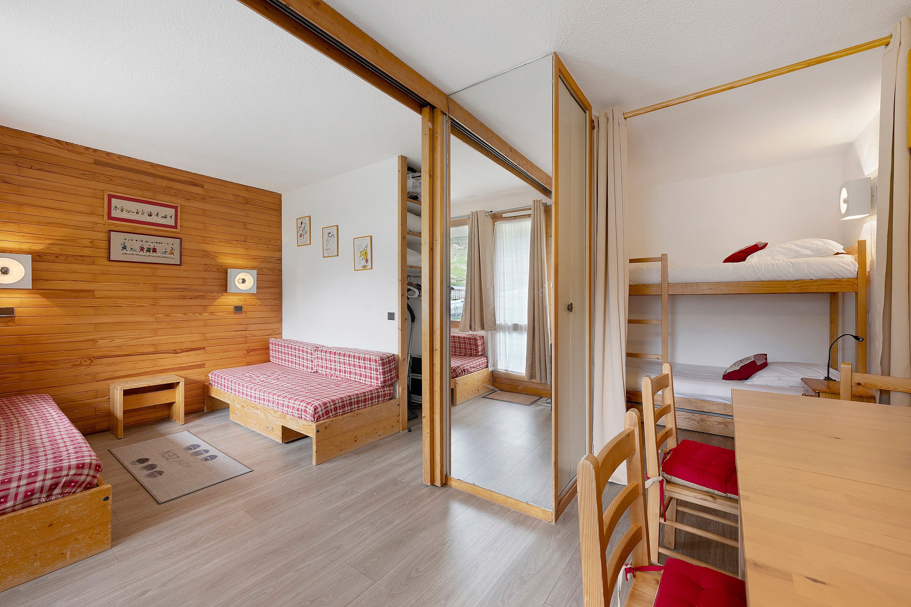 Ein kleines Zimmer mit Holzboden, einem Etagenbett, einem Einzelbett, einem Schreibtisch und einem Spiegel.