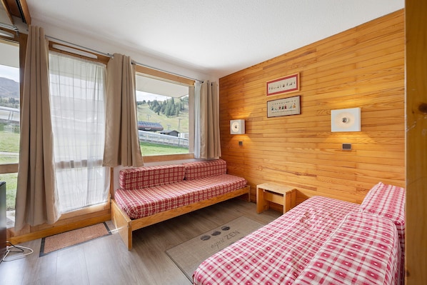 Een kamer met een houten wand, een bed, een bankje en een raam met gordijnen.