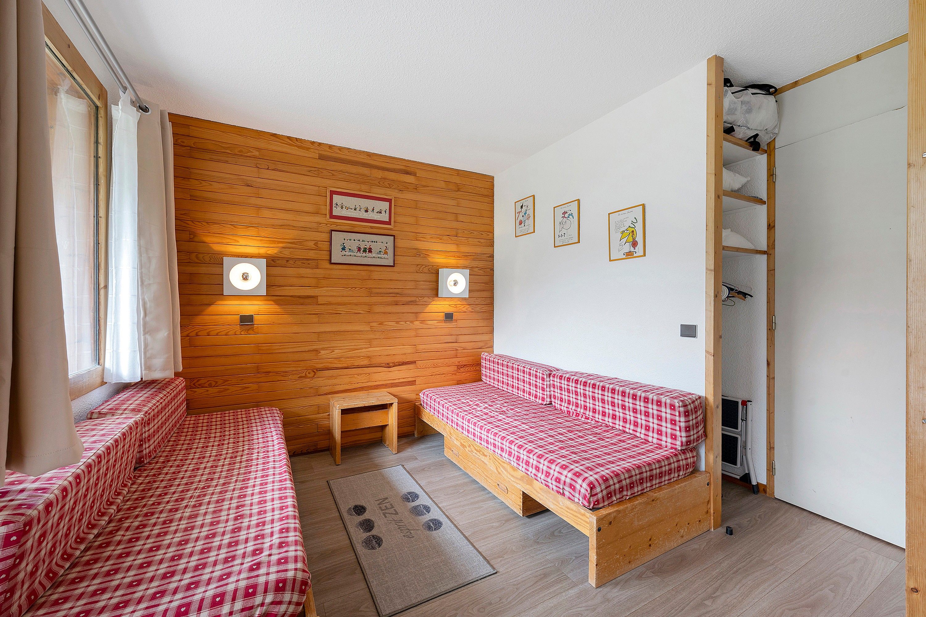 Ein Zimmer mit zwei Betten, einem kleinen Tisch und einer Holzwand mit gerahmten Bildern.