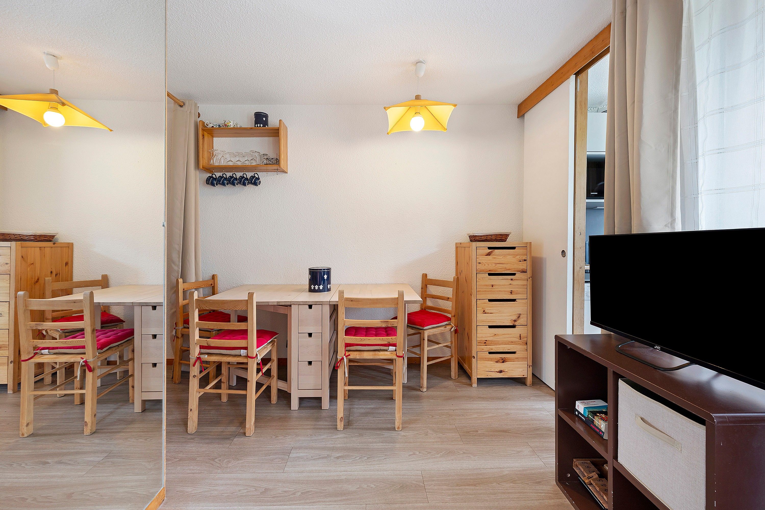 A room with a wooden table and chairs, a television, and a shelf with books.