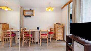 A room with a wooden table and chairs, a television, and a shelf with books.