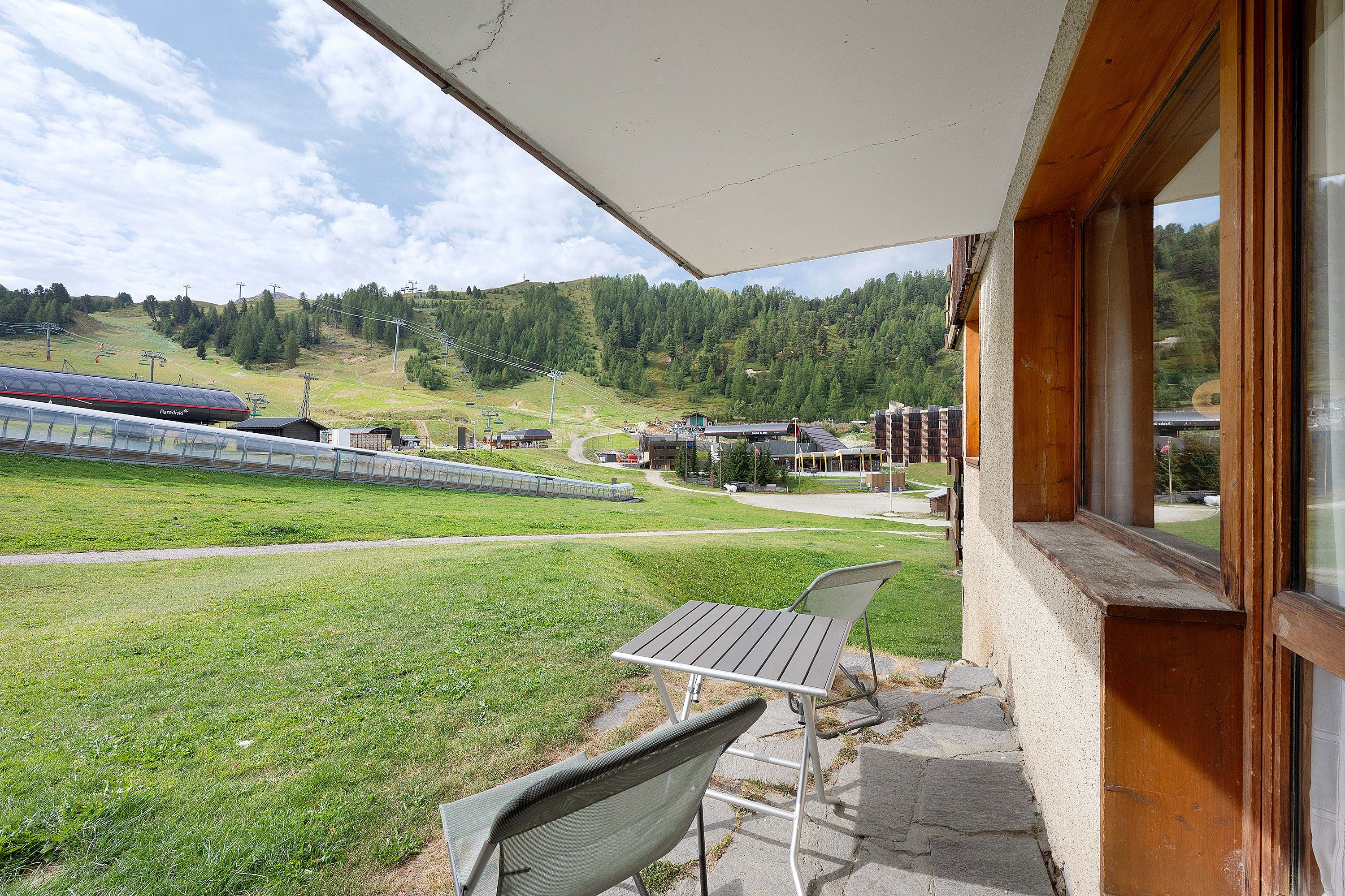 Ein überdachter Außenbereich mit Sitzgelegenheiten und Blick auf einen Skilift und eine hügelige Landschaft.