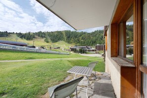 Een overdekt terras met uitzicht op een skibaan en een heuvelachtig landschap.