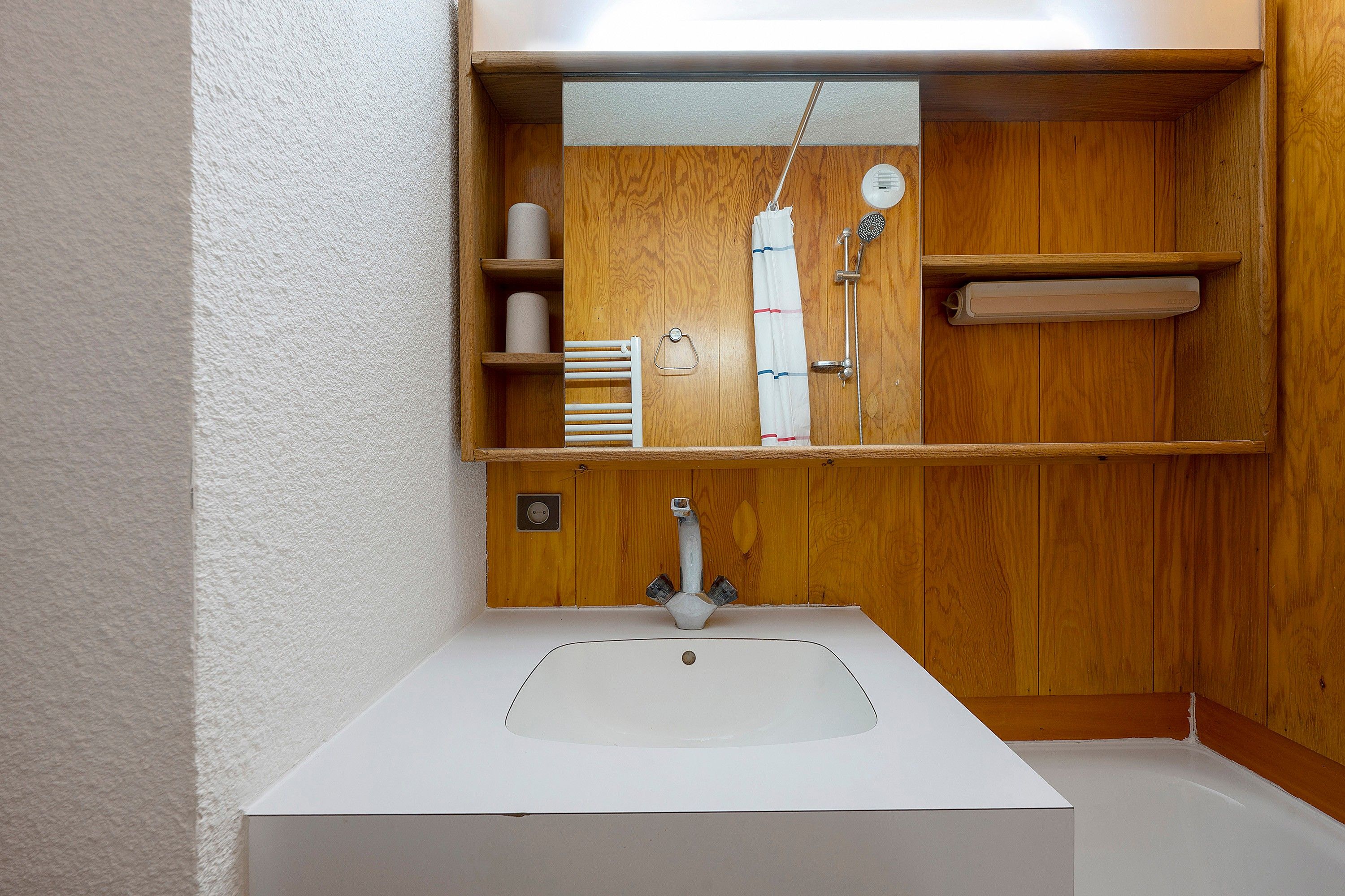 A bathroom with a white sink, wooden vanity, and a mirror.