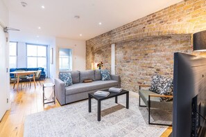 A modern living room with a brick wall, a sofa set, a coffee table, and a television. - Farringdon 1BR | Sleeps 4 | Elizabeth Line Direct (Greater London)