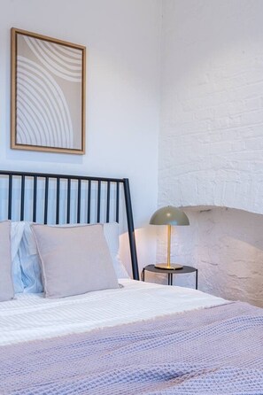 A bedroom with a bed, a nightstand, a lamp, and a wall-mounted artwork. - Farringdon 1BR | Sleeps 4 | Elizabeth Line Direct (Greater London)
