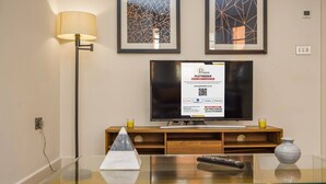 A modern living room with a glass coffee table, a flat-screen TV, a lamp, and two abstract paintings on the wall. - Fitzrovia 1BR Retreat | Near Soho & Tube-8 (Greater London)
