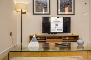 Een moderne woonkamer met een glazen salontafel, een flatscreen televisie, een lamp en twee abstracte schilderijen aan de muur.