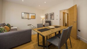 A modern living room with a dining table, grey sofa, and a wooden door. - Fitzrovia 1BR Retreat | Near Soho & Tube-8 (Greater London)