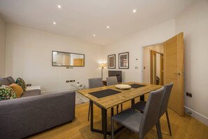 Een moderne woonkamer met een eettafel, een grijze bank en een houten deur.
