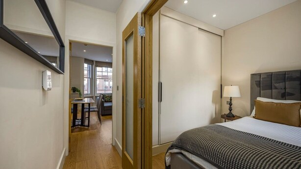 A hotel room with a bed, bedside table, lamp, and a view of the hallway. - Fitzrovia 1BR Retreat | Near Soho & Tube-8 (Greater London)