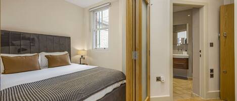 A bedroom with a bed, a nightstand, a window, and a door leading to a bathroom.