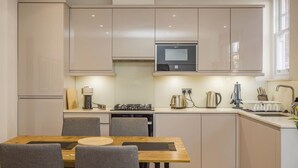 A modern kitchen with a dining table, chairs, and a built-in oven. - Fitzrovia 1BR Retreat | Near Soho & Tube-8 (Greater London)