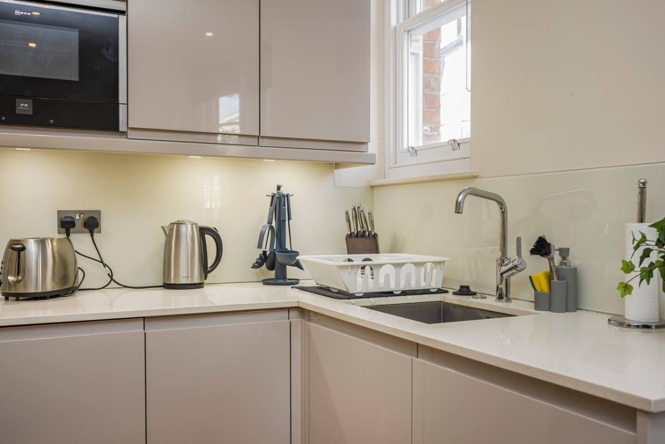 Eine moderne Küche mit integriertem Mikrowellenherd, Wasserkocher, Kaffeemaschine, Spüle mit modernem Wasserhahn und einem Fenster über der Spüle.