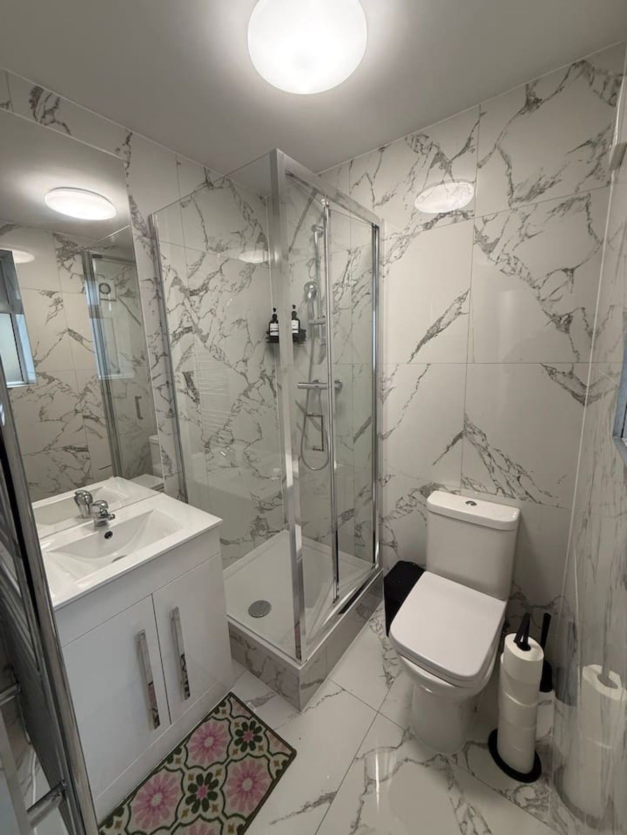 Un baño con ducha compartimentada por vidrio, lavamanos blanco y un inodoro.