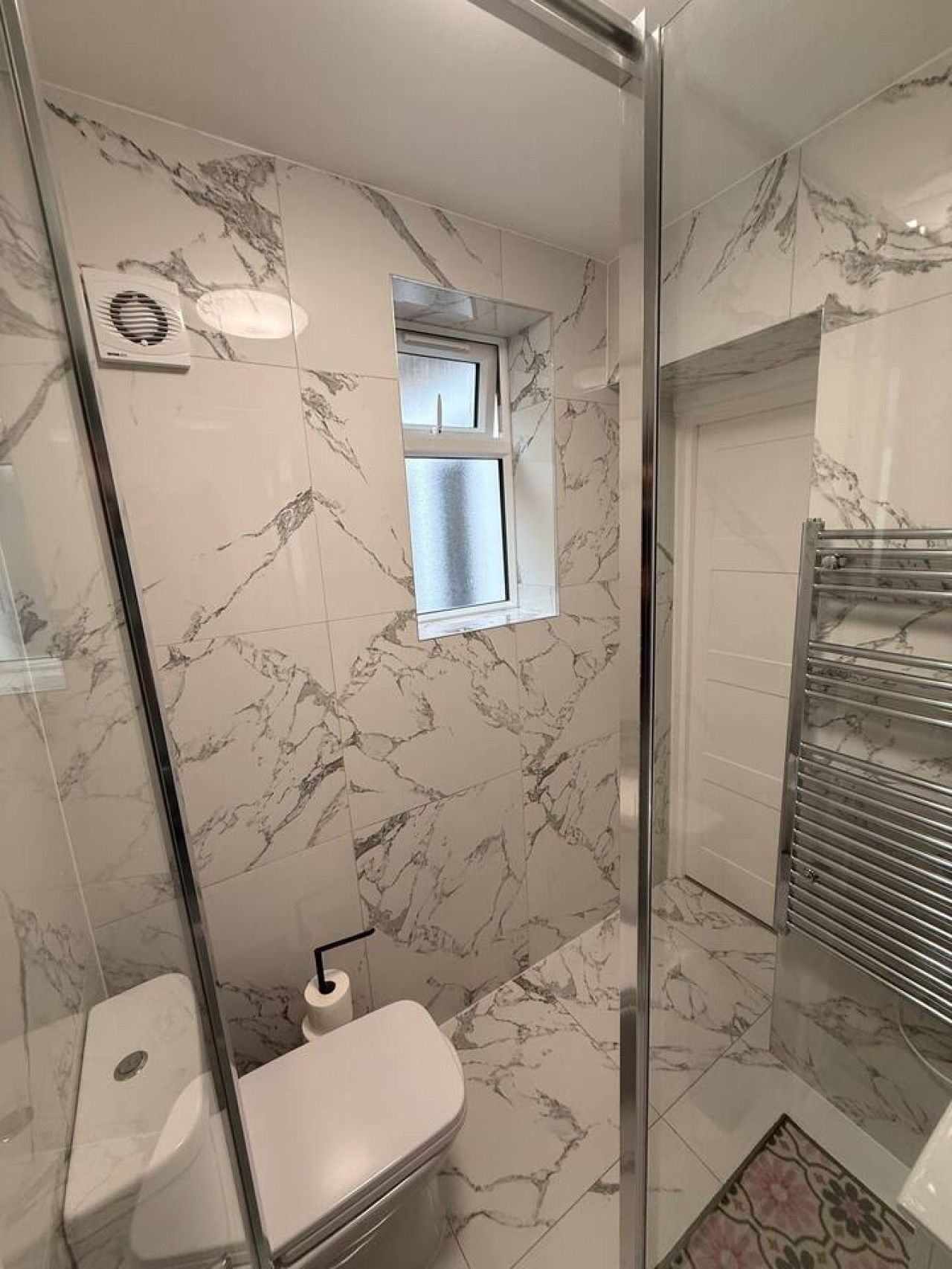 Une salle de bain avec une douche à parois de verre, des toilettes, une fenêtre et un porte-serviettes.