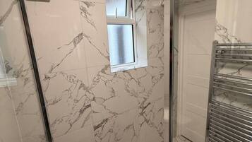 Une salle de bain avec une douche à parois de verre, des toilettes, une fenêtre et un porte-serviettes.