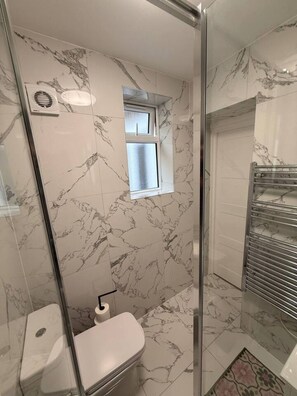 Un baño con cabina de ducha de vidrio, inodoro, ventana y perchero.