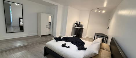 A modern bedroom with a large bed, a wardrobe, a mirror, and a small desk area.