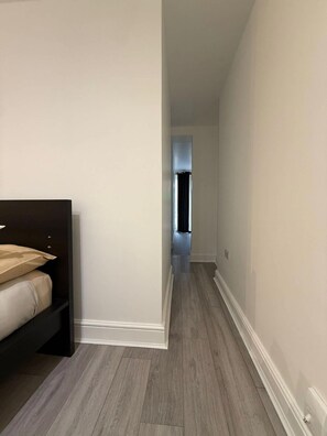 A narrow hallway with a bed on the left and a door at the end.