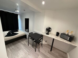 Habitación pequeña con cama, una mesita con sillas, microondas, ventilador y cafetera.