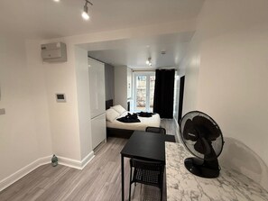 A compact room with a bed, a table, and a fan.