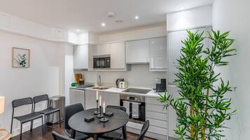 A compact kitchen with modern appliances, a dining area with a round table and chairs, and a potted plant.