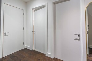 A hallway with three white doors, wooden flooring, and a plain wall. - Earl`s Court Gem | Sleeps 6 | Lift & Tube (Greater London)