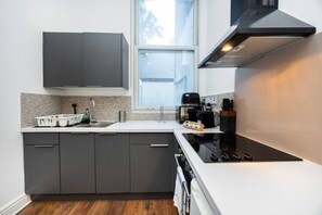 A modern kitchen with grey cabinets, a white countertop, a built-in oven, and a window above the sink. - Earl`s Court Residence | Elegant 1BR | London (Greater London)