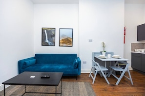 A compact living space with a blue sofa, a small dining table, and two framed pictures on the wall. - Earl`s Court Residence | Elegant 1BR | London (Greater London)