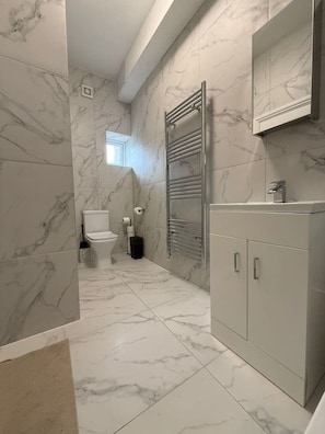 A bathroom with marble walls, a toilet, a towel rack, and a cabinet. - Modern Room | Minutes from Central London (Greater London)