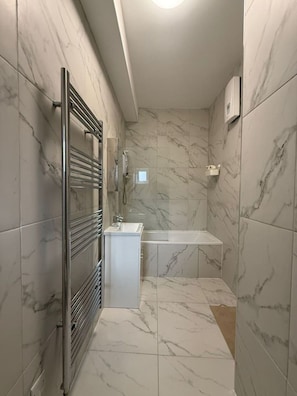 A bathroom with a glass shower enclosure, a white sink, and a marble-tiled shower area. - Modern Room | Minutes from Central London (Greater London)