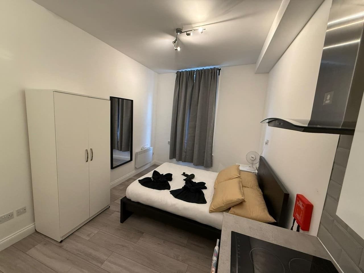 A compact bedroom with a bed, a wardrobe, a mirror, and a kitchenette.