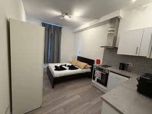 Ein kleines Hotelzimmer mit Bett, Küchenzeile und Blick nach draußen.