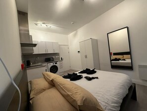 Ein Hotelzimmer mit einem Bett, einer kleinen Küchenzeile, einer Waschmaschine und einem Spiegel an der Wand.