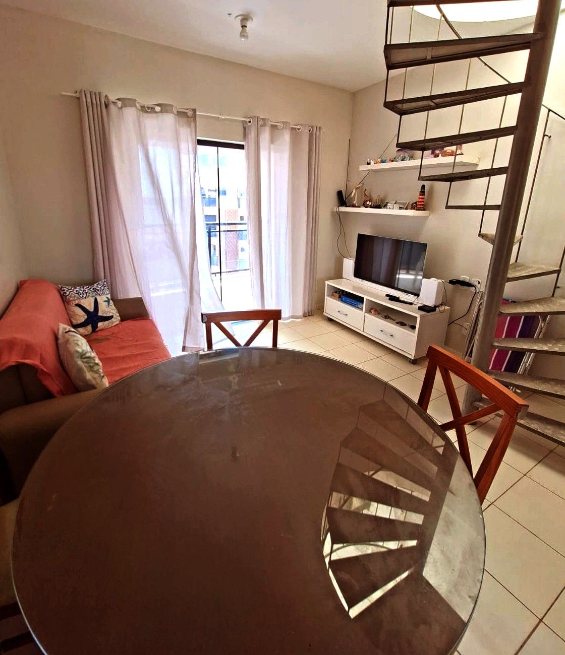Una sala de estar con una mesa redonda, un sofá, un televisor y una escalera.