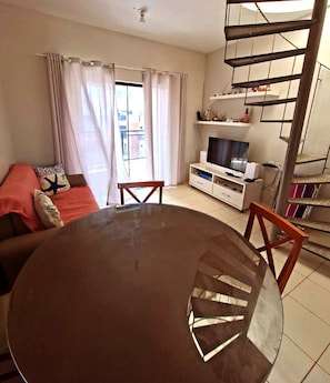 Een woonkamer met een ronde tafel, een bank, een televisie en een trap.