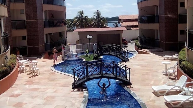 A swimming pool area with a bridge, lounge chairs, and a view of a building with multiple balconies. - SaltBeach - Cobertura Ed.Atlantic Beach (Salinópolis)