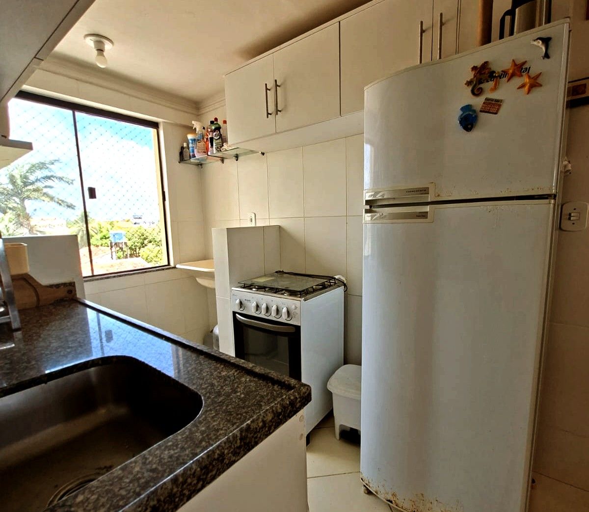 A kitchen with white cabinets, a stove, a refrigerator, and a window with a view of greenery outside.