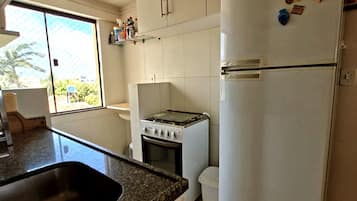 A kitchen with white cabinets, a stove, a refrigerator, and a window with a view of greenery outside.