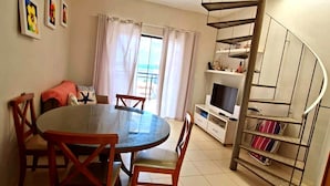 A room with a round dining table, chairs, a TV, a spiral staircase, and a view of the outdoors. - SaltBeach - Cobertura Ed.Atlantic Beach (Salinópolis)